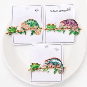 Three enamel frog and chameleon pins on branches displayed on a white plate