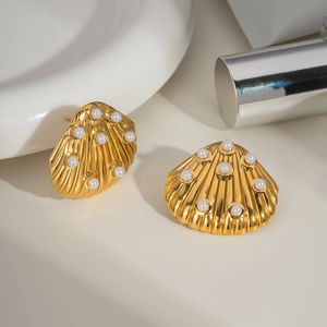 Detail shot of golden shell-shaped earrings with embedded pearls on a beige set