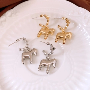Close-up of gold and silver pony charm earrings on an elegant white embossed plate