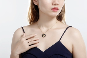 Detail of gold Hamsa Hand necklace with black circular pendant worn by a model