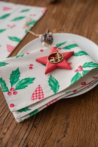 Detailed texture of Christmas holly and berry printed cotton linen table napkin on a plate