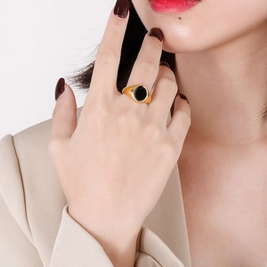 Polished gold signet ring with black oval inlay worn by a model on light beige background