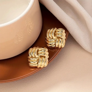 Golden square twisted knot stud earrings with woven texture on a minimalist tray