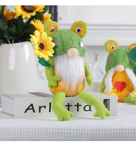 Dettaglio dello gnomo rana di peluche con cappello verde e un fiore di girasole in mano