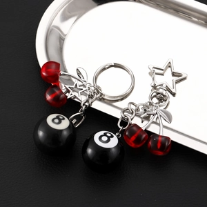 Detail of red cherry and number 8 pool ball keychains with star charms on metallic tray