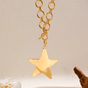 Detail of gold star pendant necklace with thick chain and toggle clasp on beige background