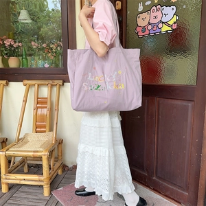 Détail du sac cabas en toile violette avec broderie colorée porté par un mannequin au café
