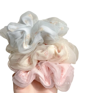 Tre elastici per capelli in rete con margherite blu, beige e rosa tenuti in mano