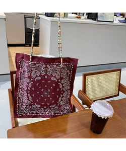 Detail of burgundy paisley tote bag with woven handles hanging on a wooden chair