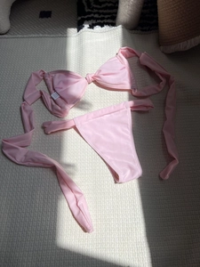 Flat lay of pink two-piece bikini with tie-knot top and matching bottoms on waffle rug