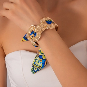 Detail of a gold metallic bangle with intricate scales and woven blue floral silk ribbon