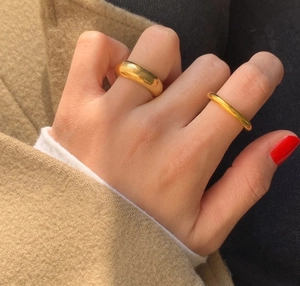 Detail of polished gold wide and slim minimalist stacking rings on person wearing wool coat