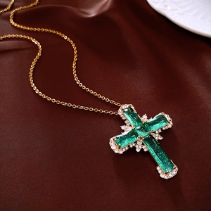 Collier croix dorée vintage avec pierres vert émeraude et zircons sur tissu en satin