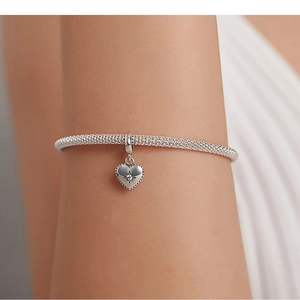 Detailed close-up of a silver heart charm bracelet with starburst engraving and zircon