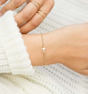 Close-up of a delicate gold-tone cross bracelet worn on a wrist against white knitwear