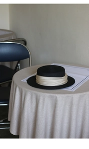 Close-up of black flat top boater hat featuring a champagne silk ribbon and woven straw texture