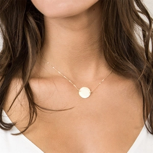 Close-up of minimalist gold circular pendant necklace worn by a fashion model