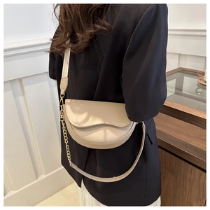 Detailed view of a beige crescent saddle bag with a wide strap and gold chain detail