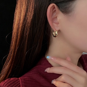 Detail of gold-plated hammered texture hoop earrings worn by a model in soft side light