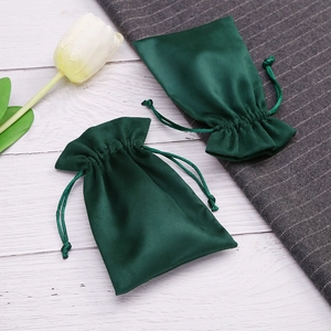 Detail of dark green velvet drawstring jewelry bags displayed on a wooden surface with a tulip