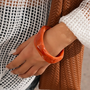 Close-up of a wide resin bangle in amber orange with marble texture and glossy finish