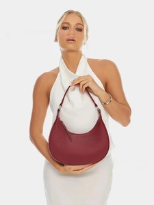 Close-up of burgundy lychee-grain crescent bag held by a model on white background