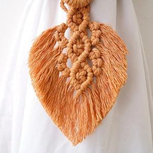 Detail of handmade orange woven cotton leaf curtain tieback with macrame texture