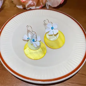 Floral hoop earrings with white petals and yellow shell pendants in a ceramic tray