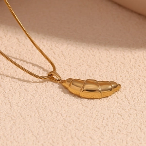 Close-up of 18K gold plated croissant pendant with sleek snake chain on beige background