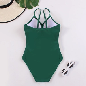 Flat lay of a dark green one-piece swimsuit with cross back straps and summer accessories