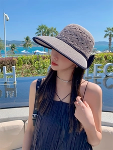 Detailed view of women's straw sun hat with a large black bow against a seaside background