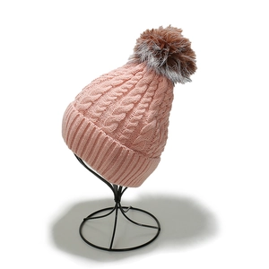 Detail of pink knitted winter beanie with a brown faux fur pompom on a display stand
