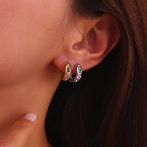 Close-up of geometric gold and silver earrings with colorful emerald and pear-cut zircons