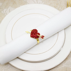 Close-up of golden heart napkin ring with red rhinestones on a white napkin