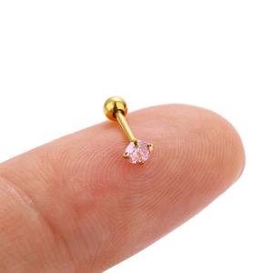 Macro shot of a small gold piercing earring with pink zircon shown on a fingertip