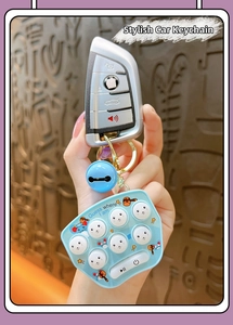 Blue mini whack-a-mole game keychain with bell held in hand against brown wall