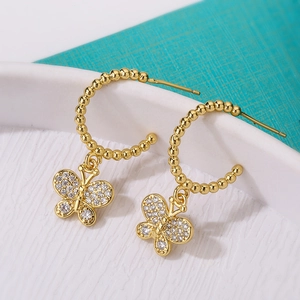 Gold-plated butterfly drop earrings with zircon crystals on a textured white plate