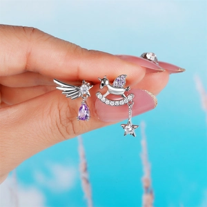Macro view of silver angel wing and unicorn rocker earrings with purple gemstones