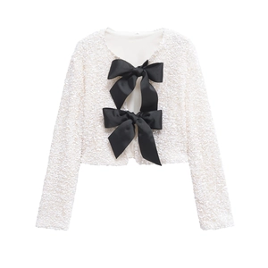 Primer plano de chaqueta blanca con lentejuelas y grandes lazos negros decorativos