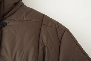 Détail d'une veste matelassée marron avec texture mate et boutons noirs ronds