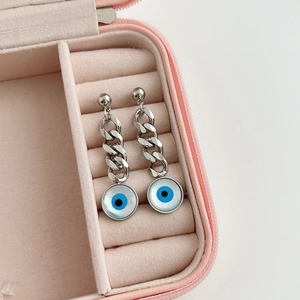 Détail des boucles d'oreilles œil de démon avec chaîne cubaine dans une boîte rose