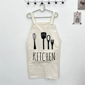 Detail of off-white canvas kitchen apron featuring cutlery graphics and H-shaped straps