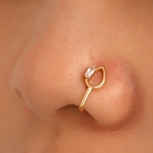 Close-up of gold nose cuff featuring a rectangular clear zircon in a geometric U-shape