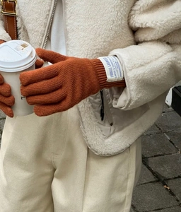 Detalle de guantes táctiles de lana naranja-marrón con etiqueta tejida y punto