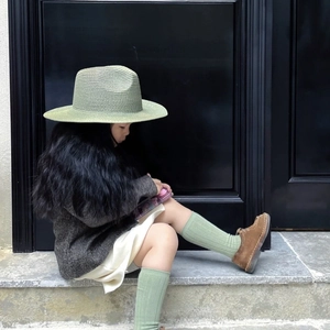 Outdoor shot of kid in sage green straw hat and knit set on stone steps