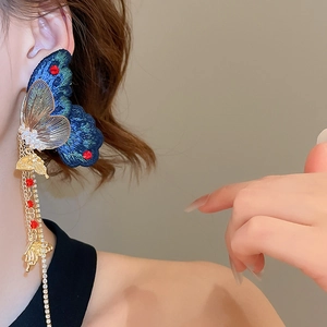 Détail de la boucle d'oreille papillon brodée bleue avec glands dorés et strass brillants