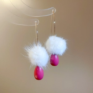 Dettaglio di eleganti orecchini con pompon bianchi e pendenti a goccia fucsia