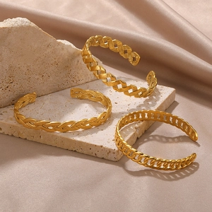 Three gold stainless steel open bangles with woven and chain link hollow designs on stone