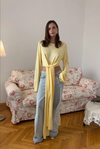 Dettaglio di un crop top in maglia giallo chiaro con lunghi nastri a fiocco e maniche snelle