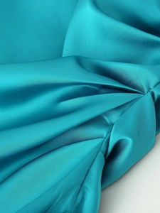 Macro shot of teal satin fabric showing smooth texture and elegant pleated details
